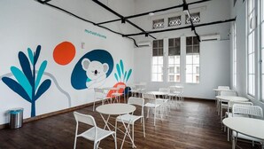 Una habitación amplia con mobiliario blanco, un mural con formas abstractas y ventanas grandes.