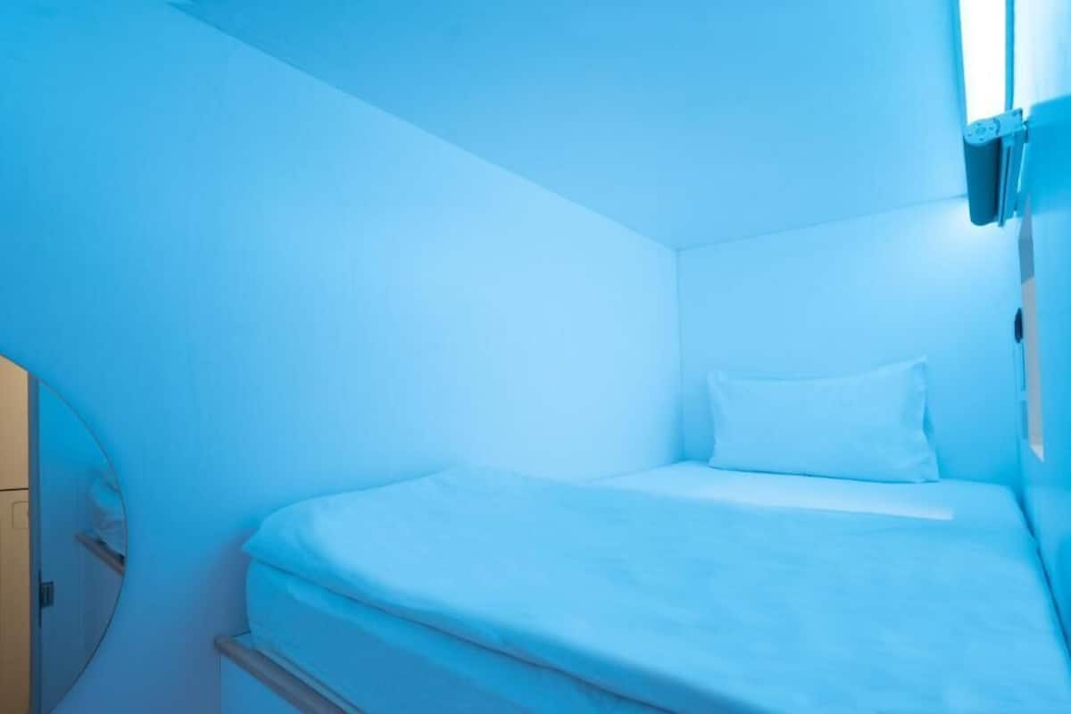 A small, compact room with a single bed and a bedside table.