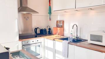 Een moderne keuken met witte kastjes, roestvrijstalen apparatuur, een houten aanrechtblad en een inbouwoven.