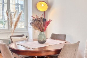 Ein runder Esstisch mit einer Vase getrockneter Blumen, einer Lampe und Stühlen.