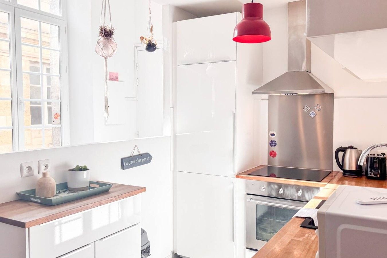 A modern kitchen with white cabinetry, a stainless steel range hood, a wooden countertop, and a red pendant light.