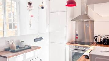 A modern kitchen with white cabinetry, a stainless steel range hood, a wooden countertop, and a red pendant light.