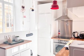 Una cocina moderna con armarios blancos, una campana extractora de acero inoxidable, una encimera de madera y una lámpara colgante roja.