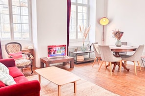 Ein Wohnzimmer mit Fernseher, einem Esstisch und einem roten Sofa.