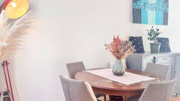 Un coin repas avec une table ronde, six chaises, un vase contenant des fleurs séchées, une lampe et un tableau accroché au mur.