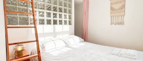A bedroom with a bunk bed, a ladder, a bedside lamp, a wall hanging, and a window with curtains.
