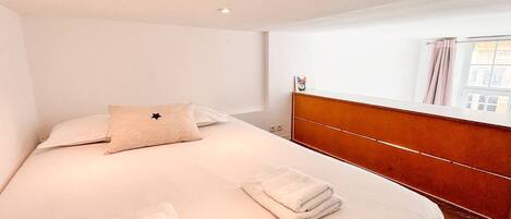 A hotel room with a bed, a headboard, a window with curtains, and a bedside table.