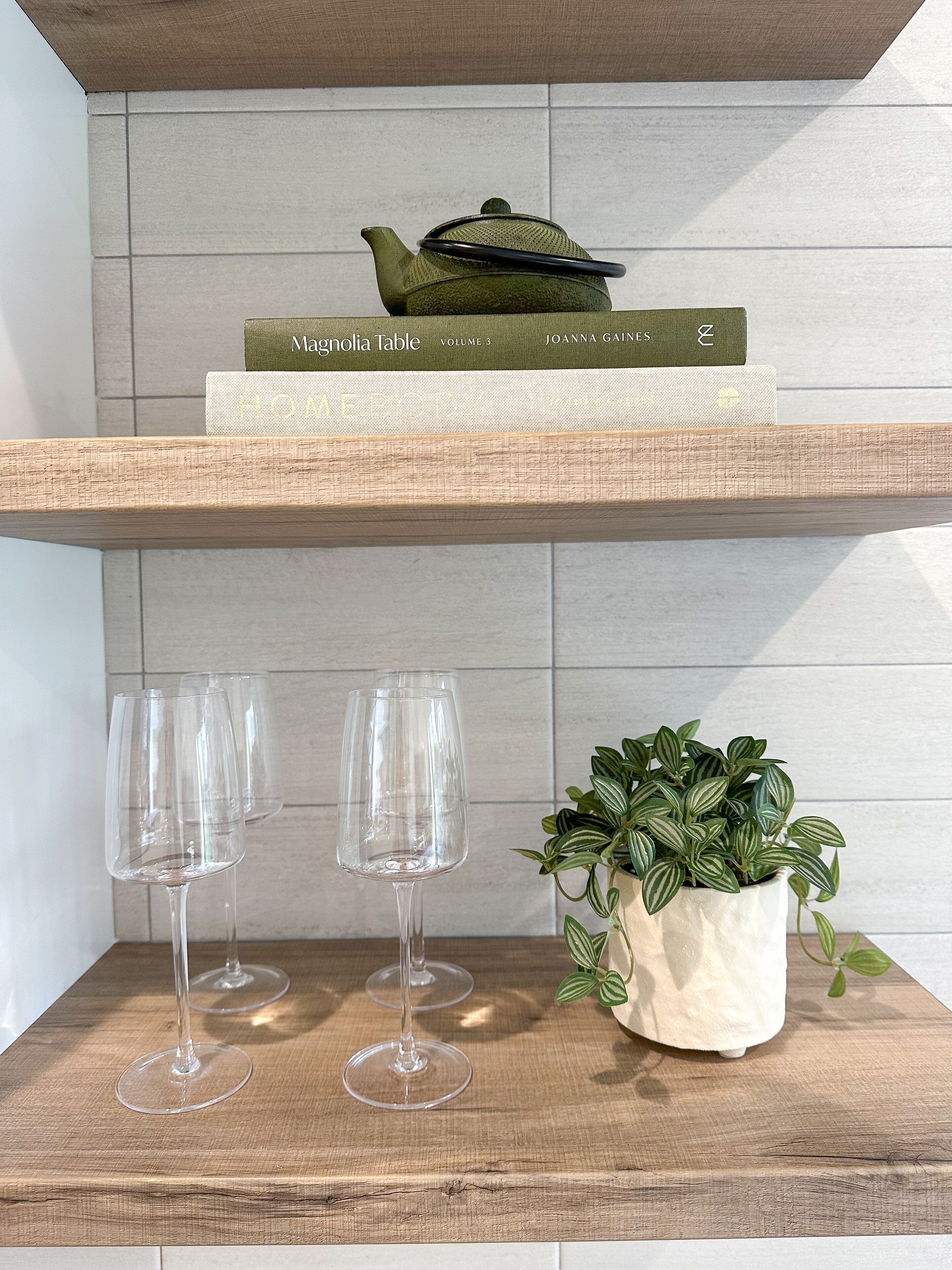 Una estantería de madera con un hervidor verde, un libro titulado 'Magnolia Table Volumen 3' y una planta en maceta.