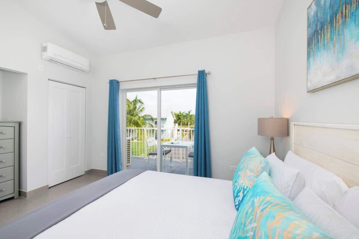A hotel room with a bed, a desk, a chair, a window with curtains, and a ceiling fan.