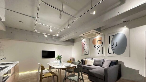 En moderne stue med spiseplads, en grå sofa og abstrakt vægkunst.