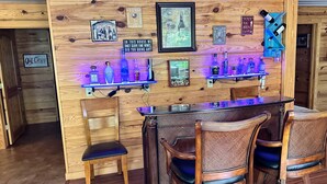A bar area with wooden walls, a bar counter, and two wicker chairs.