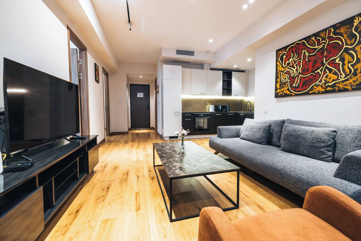 Una sala de estar moderna con un televisor de pantalla plana, un sofá, una mesa de centro y una cocina al fondo.