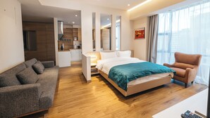 A modern hotel room with a bed, a sofa, a chair, a desk, and a kitchenette. - May Seven Hotel and Suites (Ulaanbaatar)
