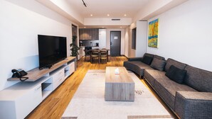 A modern living room with a flat-screen TV, a wooden coffee table, a grey sofa, and a kitchen in the background. - May Seven Hotel and Suites (Ulaanbaatar)