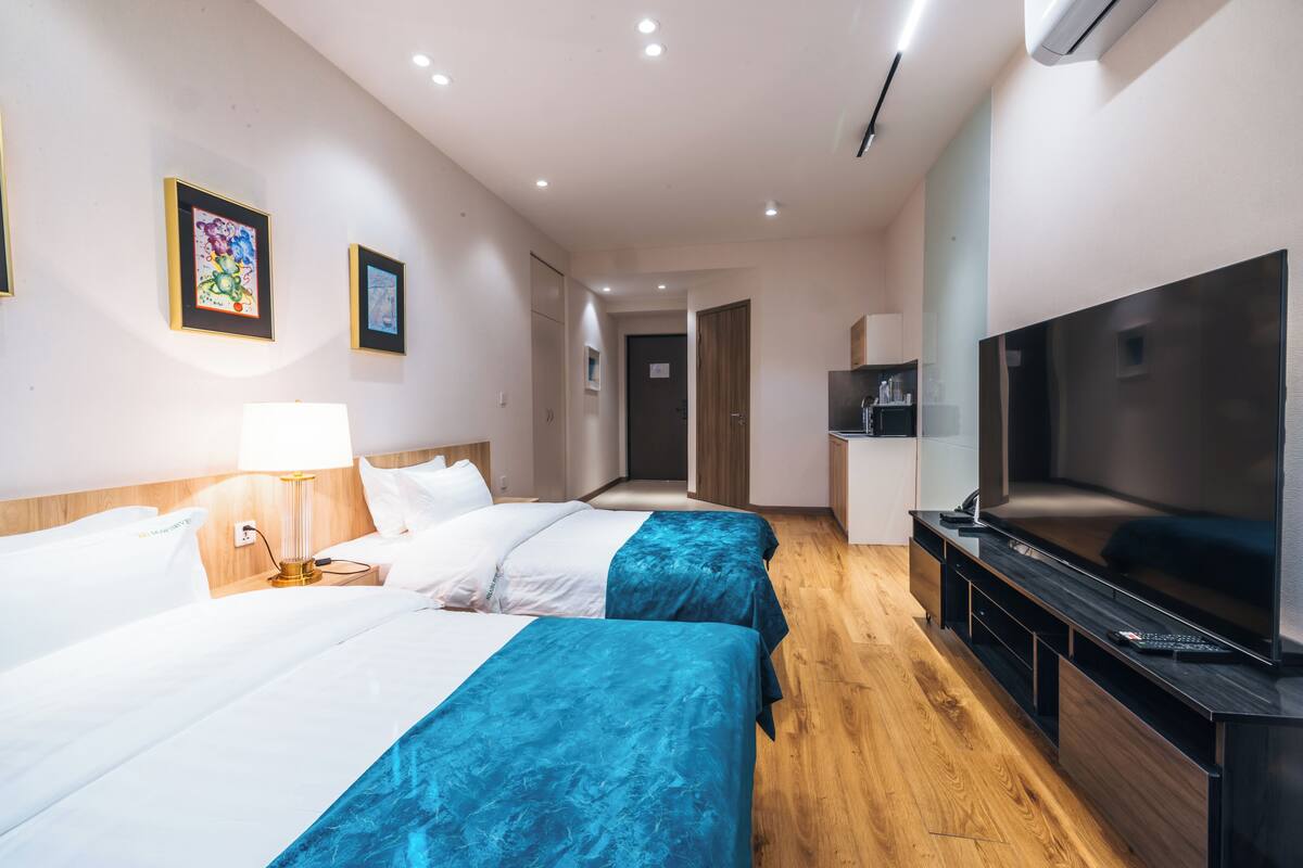 Habitación de hotel con dos camas, televisión, escritorio y kitchenette.