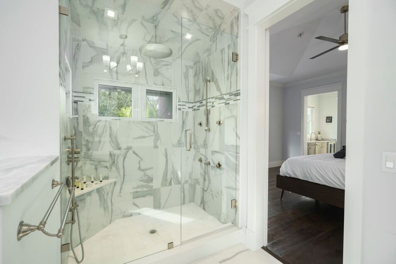 Une salle de bain moderne avec une douche à parois de verre, des murs en marbre et un espace lavabo bien visible.