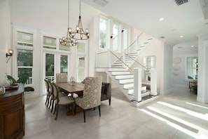 A spacious dining area with a large table and chairs, a chandelier, and a staircase leading to an upper level. - Upscale 6BR Mansion w/ Pool & Hot Tub (Stuart)