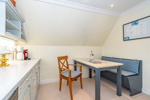 A small, cozy room with a wooden chair, a table, and a bench. There is a coffee machine on the counter, and a framed picture on the wall. - Admiralswohnung - Friesische 3-zimmerwohnung. - nur 300 Meter zum Watt (Sylt)