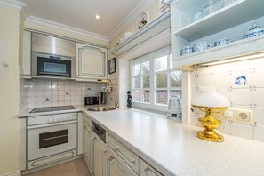 A kitchen with white cabinetry, a stainless steel oven, a microwave, and a window with a view of a brick building.