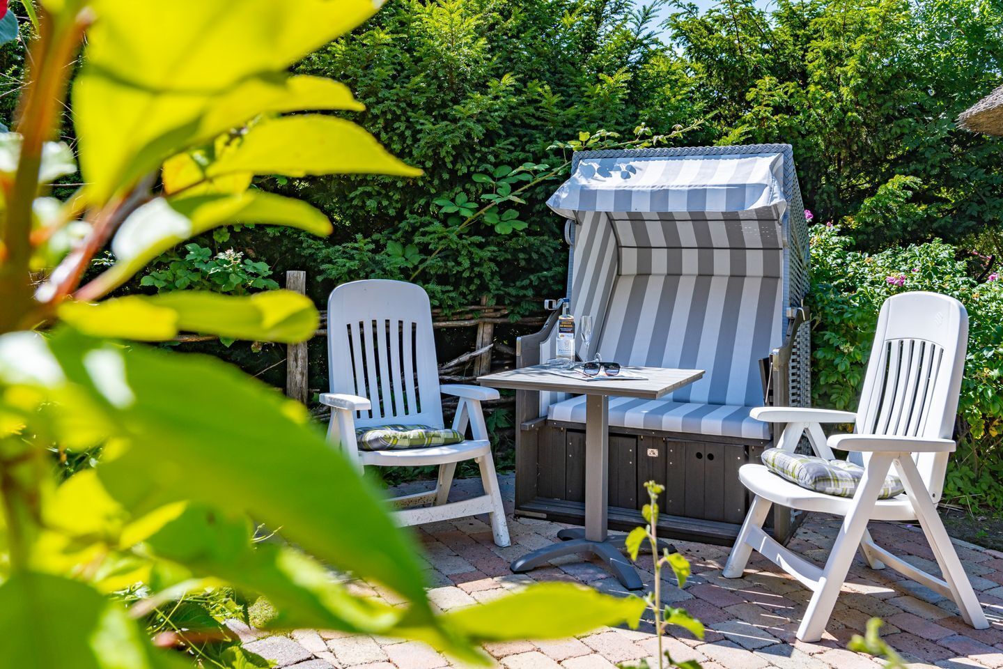 An outdoor patio with a striped awning, two white chairs, and a table.