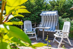 An outdoor patio with a striped awning, two white chairs, and a table.