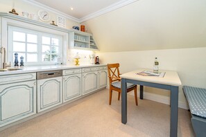 Una cocina con muebles blancos, una mesa de comedor y una silla.