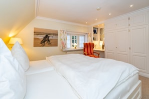 A bedroom with a bed, a chair, a window with curtains, a painting on the wall, and a wardrobe.
