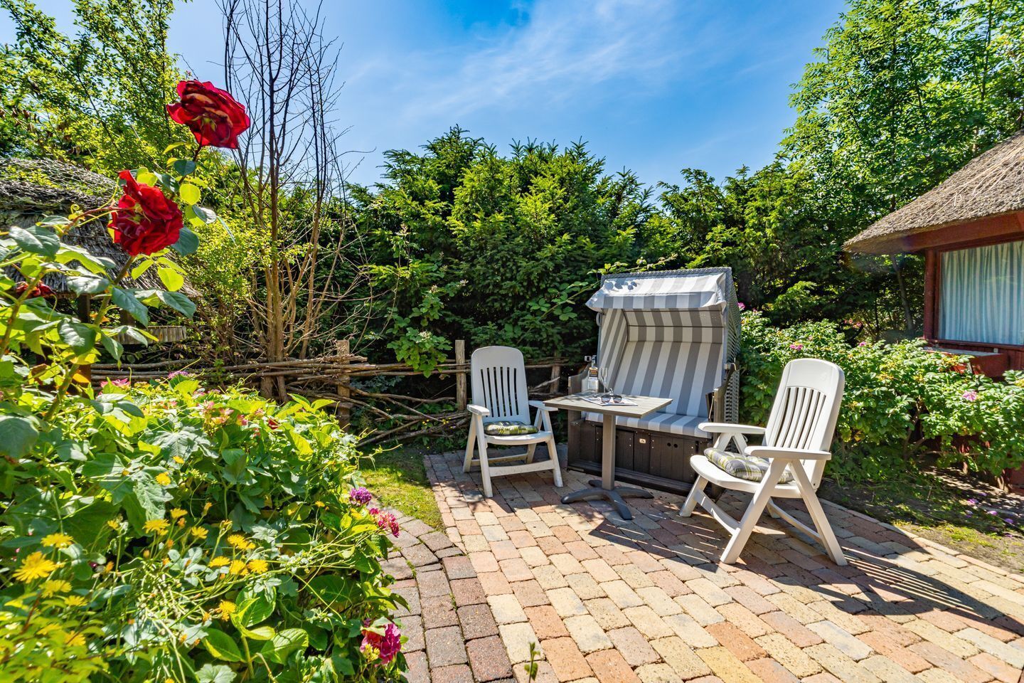 Une terrasse avec une table et deux chaises, entourée d’une végétation luxuriante et d’une structure à toit de chaume.