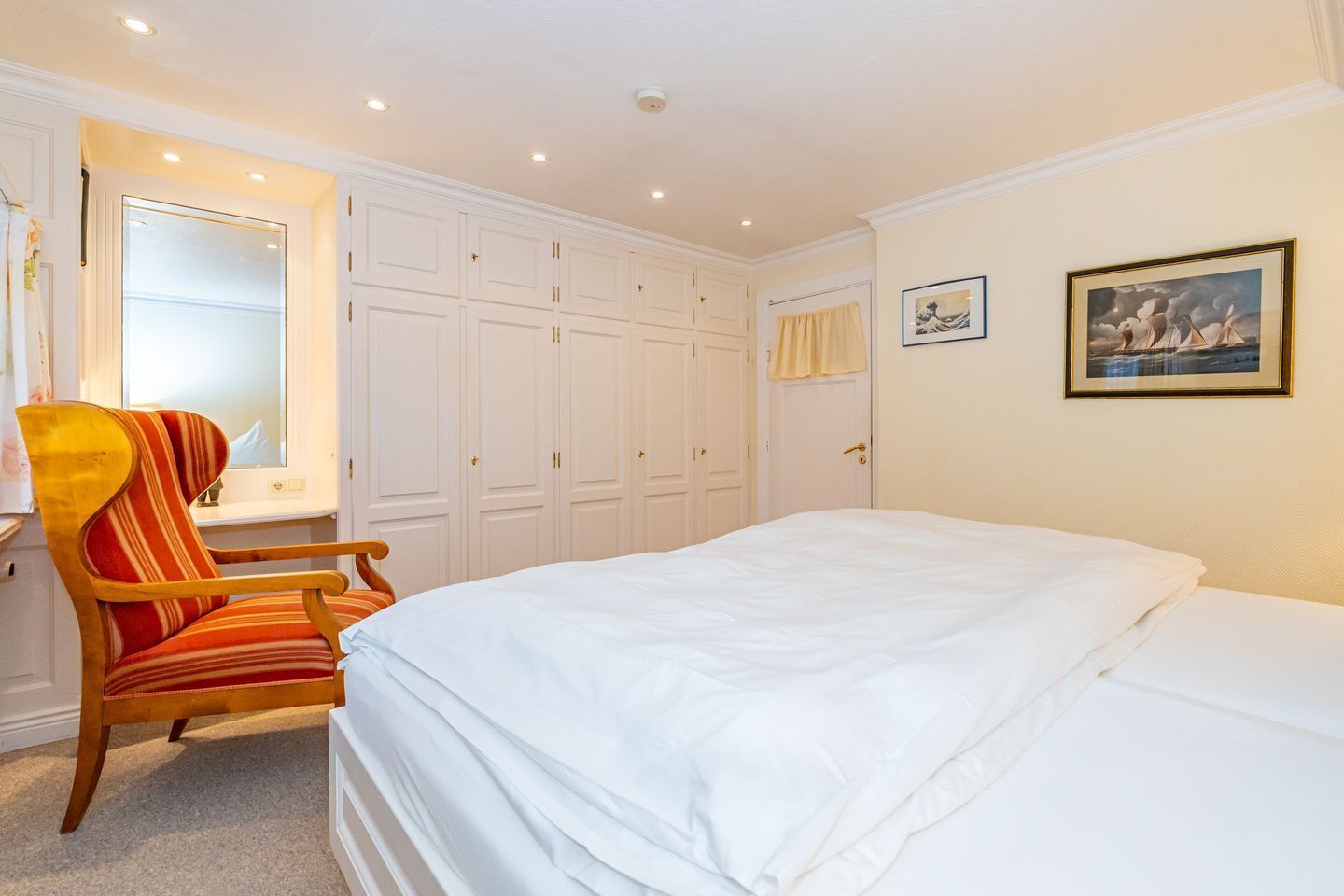 A hotel room with a bed, a chair, a wardrobe, and a painting on the wall.
