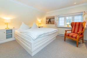 A bedroom with a large bed, bedside lamps, a window with curtains, and a striped armchair.
