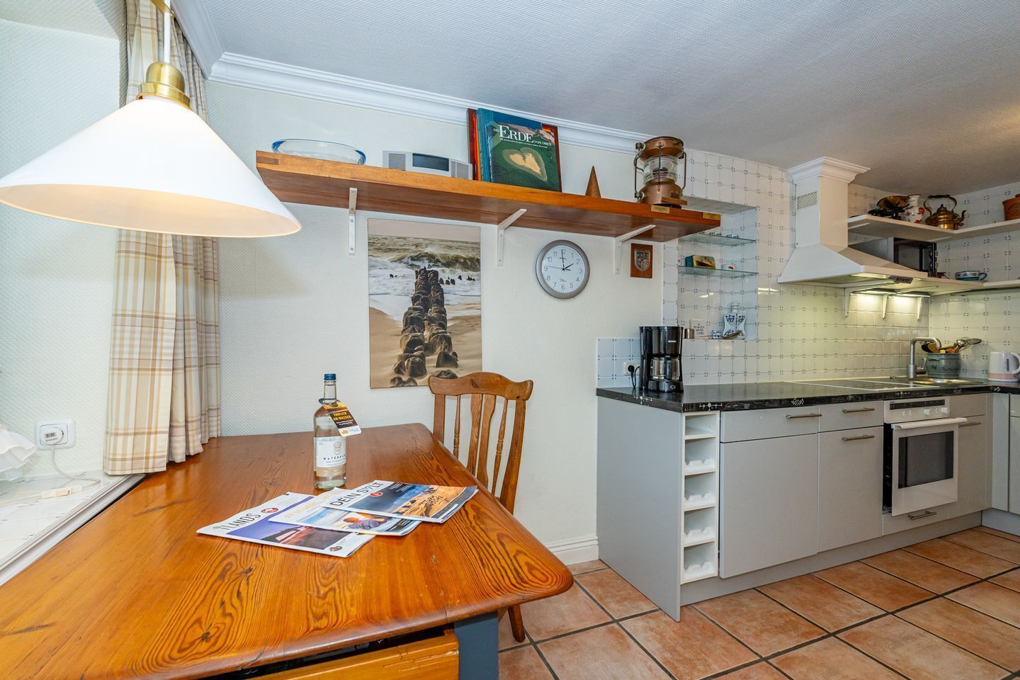 A compact kitchen with white cabinets, a wooden dining table, a clock, and a coffee maker.