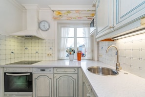 A kitchen with white cabinetry, a stainless steel sink, a clock, and a window with curtains.