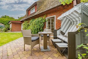 A patio with wicker furniture, a brick house, and a thatched roof. - Kajüte - Friesische 2-zimmerwohnung mit Terrasse (Sylt)
