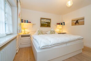Une chambre à coucher avec un grand lit, deux tables de chevet avec des lampes, un radiateur et une fenêtre avec des rideaux.