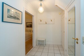 A hallway with a framed picture of a ship, a small bench, and a door with a golden handle. - Kajüte - Friesische 2-zimmerwohnung mit Terrasse (Sylt)