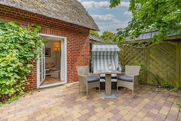 A brick house with a thatched roof, a patio with wicker furniture, and a wooden gate.
