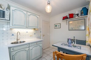 A kitchen with white cabinets, a sink, and a dining area with a table and chairs. - Kajüte - Friesische 2-zimmerwohnung mit Terrasse (Sylt)
