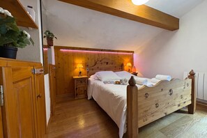 A bedroom with a wooden bed, bedside lamps, a nightstand, and a potted plant.