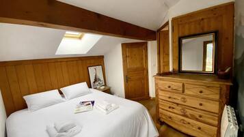 Un dormitorio con cabecera de madera, cama con ropa blanca, cómoda, espejo y tragaluz.