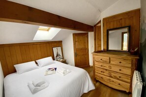 Een slaapkamer met een houten hoofdbord, een bed met witte lakens, een dressoir, een spiegel en een dakraam.