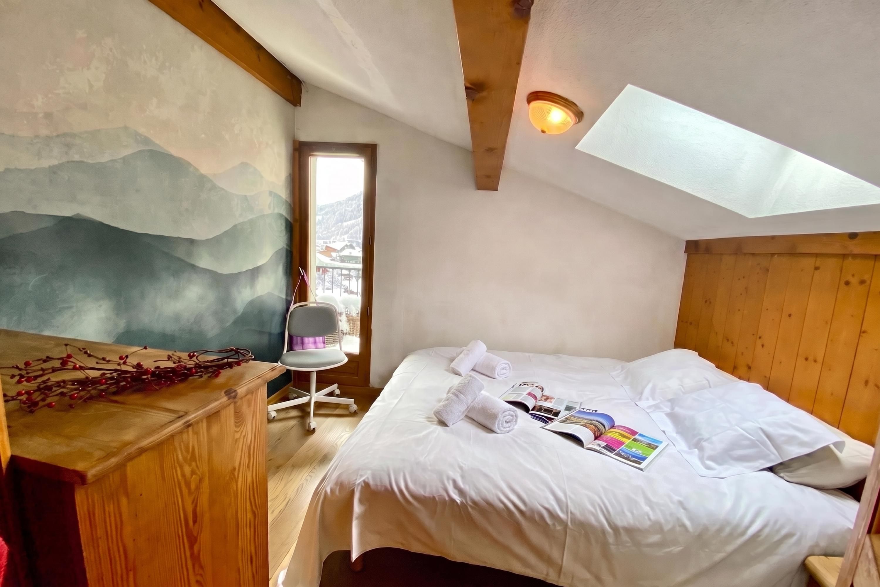 Une chambre à coucher avec un lit, un bureau, une chaise, un tableau et une lucarne.