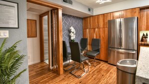 A modern kitchen with wooden cabinets, a stainless steel refrigerator, and a dining area with black chairs.