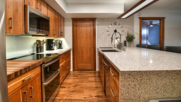 A modern kitchen with wooden cabinets, a granite countertop, a built-in microwave, and a wall clock.
