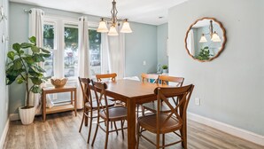 A dining area with a wooden table and chairs, a chandelier, and a potted plant. - Steps to Beach | Backyard | Shuffle Board (Hampton)