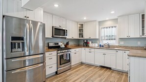 A modern kitchen with stainless steel appliances, white cabinetry, and a wooden floor. - Steps to Beach | Backyard | Shuffle Board (Hampton)