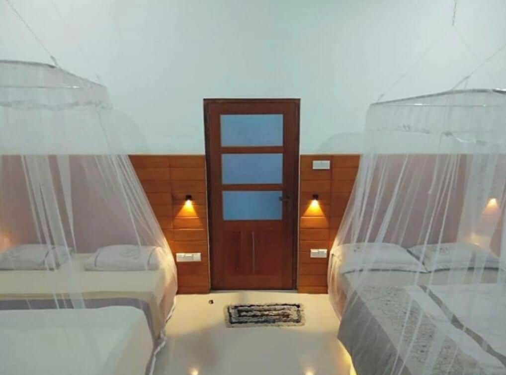 A room with two beds, each with a canopy, a wooden door with glass panels, and wall-mounted lights.