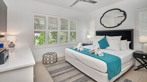 A modern bedroom with a bed, bedside tables, a ceiling fan, and a large window with blinds. - 1 Bedroom Apartment Beach Club Palm Cove (Palm Cove)