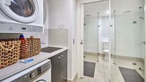 A compact laundry area with a washing machine, dryer, and a wicker basket on the countertop. - 1 Bedroom Apartment Beach Club Palm Cove (Palm Cove)