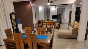 Un salon comprenant un coin repas, des meubles en bois, un ventilateur de plafond et un téléviseur.