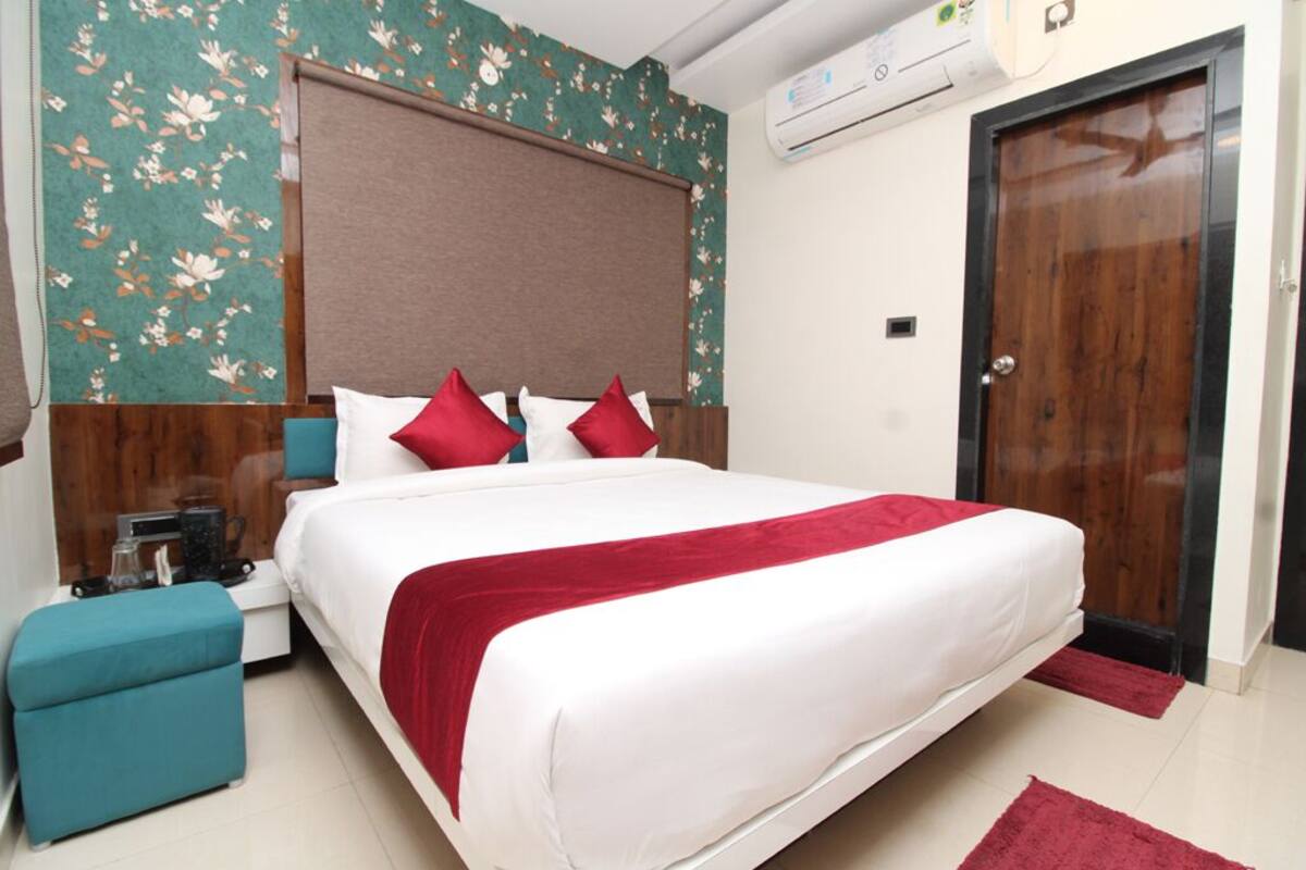 Habitación de hotel ordenada con una cama grande, cabecera de madera, una pequeña zona de estar y una puerta.
